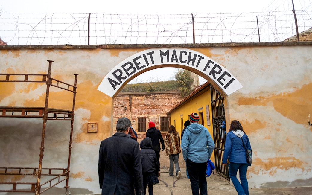 Tourists entering Terezin Concentration Camp under "Arbeit Macht Frei" sign.