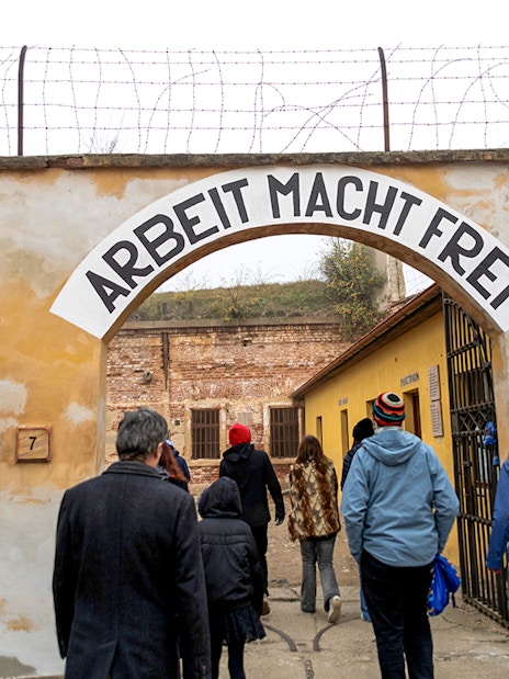 Tourists entering Terezin Concentration Camp under "Arbeit Macht Frei" sign.