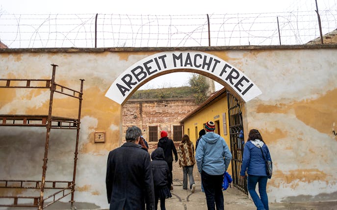 Tourists entering Terezin Concentration Camp under "Arbeit Macht Frei" sign.