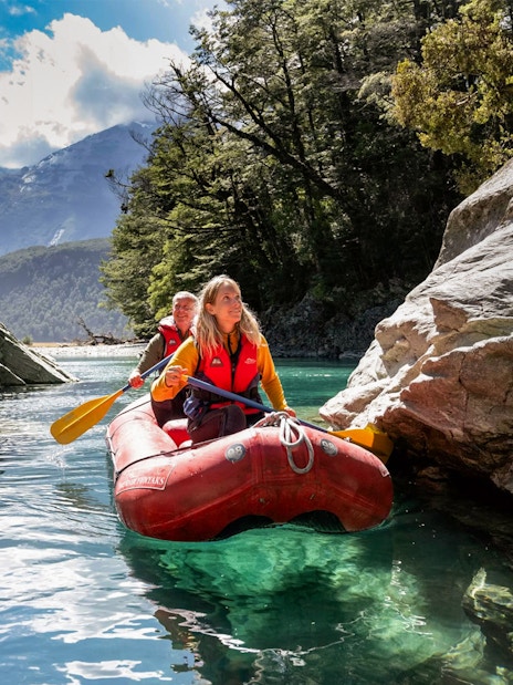 Two people paddling a red inflatable kayak on Dart River, surrounded by rocky cliffs and forest.