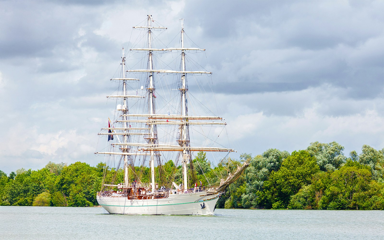 Tall ship Shabab Oman II sailing on the Seine River in Paris, France, with iconic cityscape in the background.