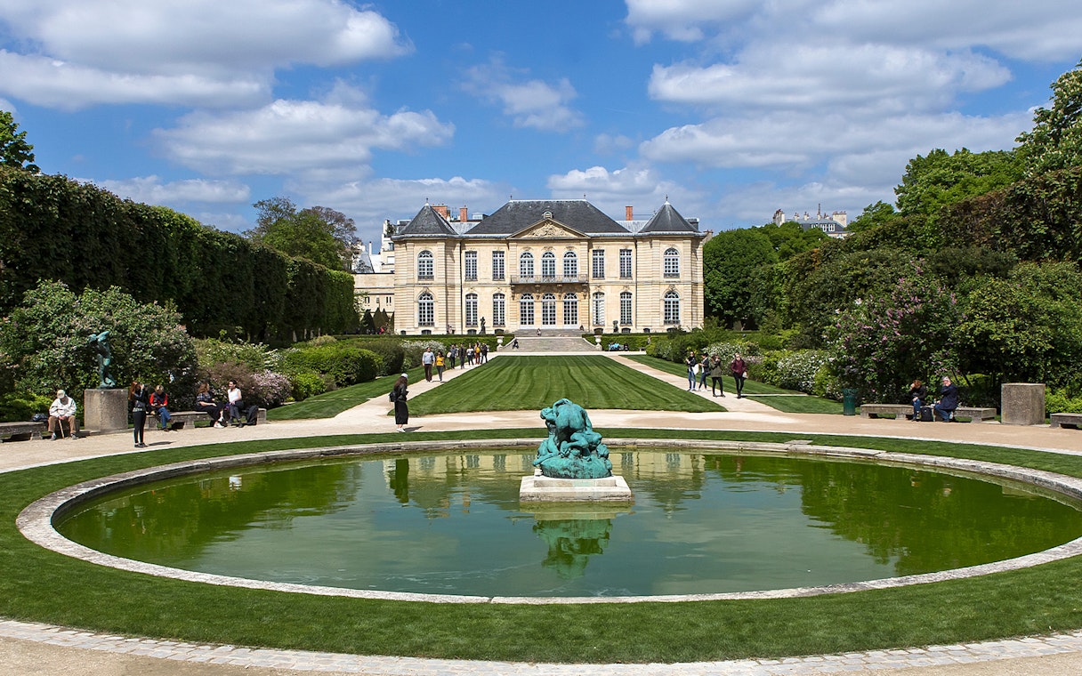 Visitors at the Rodin Museum gardens in Paris, viewing sculptures and the historic building.