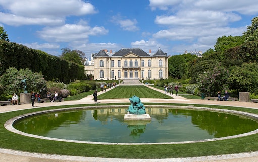 Visitors at the Rodin Museum gardens in Paris, viewing sculptures and the historic building.