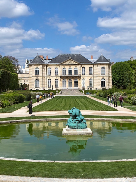 Visitors at the Rodin Museum gardens in Paris, viewing sculptures and the historic building.