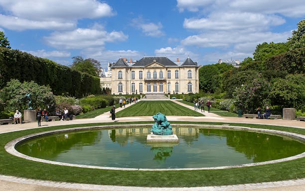 Visitors at the Rodin Museum gardens in Paris, viewing sculptures and the historic building.