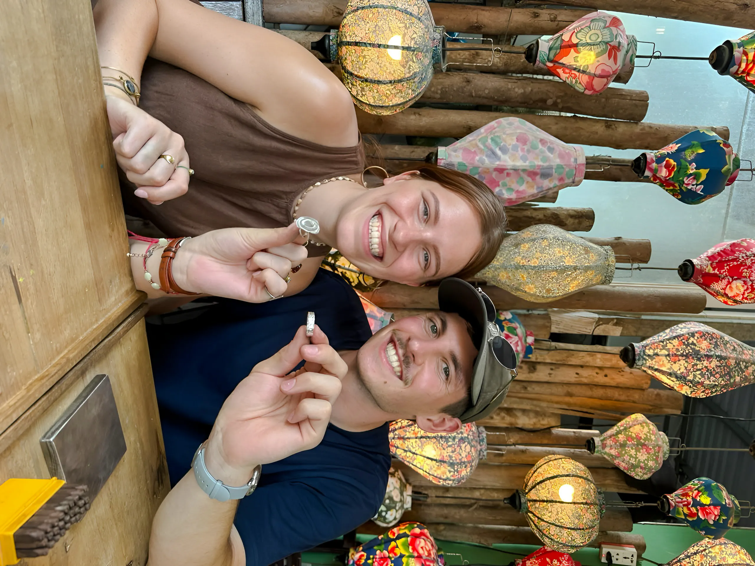 Couple crafting jewelry in Hoi An workshop with colorful lanterns in the background.