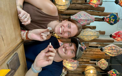 Couple crafting jewelry in Hoi An workshop with colorful lanterns in the background.