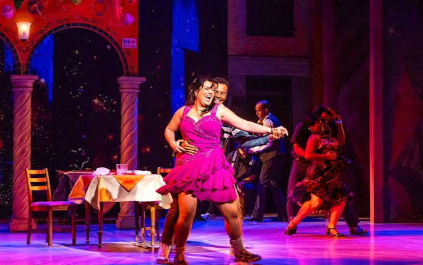 Dancers performing in "Real Women Have Curves: The Musical" on a vibrant stage.