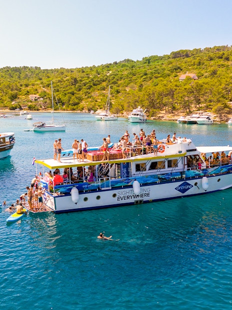 Tourists enjoying a boat cruise in the Blue Lagoon, Šolta, with surrounding yachts and lush greenery.