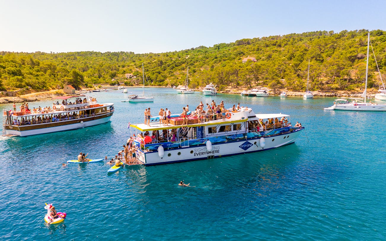Tourists enjoying a boat cruise in the Blue Lagoon, Šolta, with surrounding yachts and lush greenery.