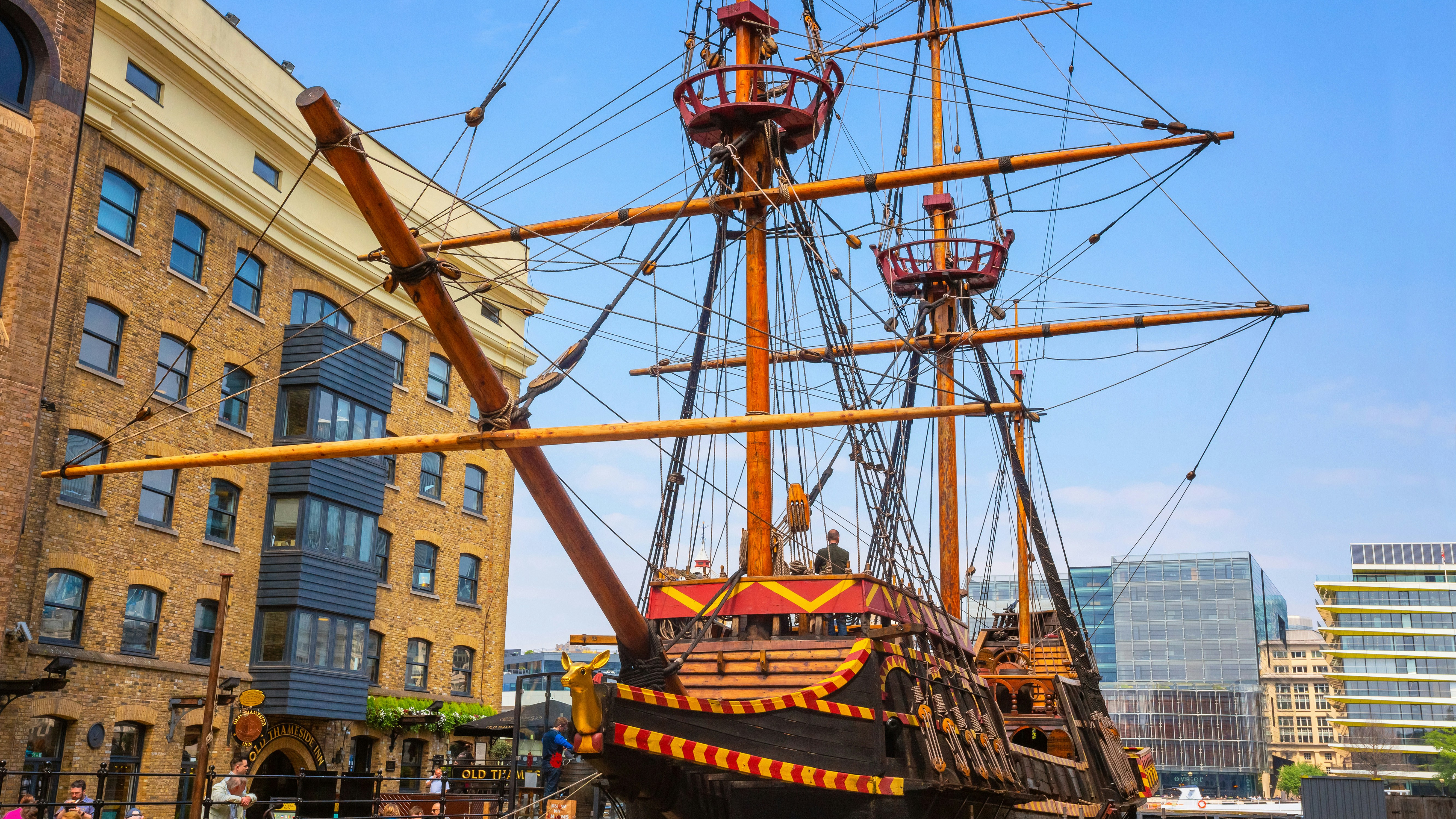 Replica of the Golden Hinde ship docked in London, UK, near historic buildings.