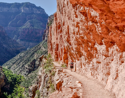Hiker on North Kaibab Trail in Roaring Springs Canyon, Grand Canyon, passing through red limestone tunnel.