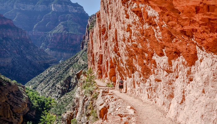 Hiker on North Kaibab Trail in Roaring Springs Canyon, Grand Canyon, passing through red limestone tunnel.C