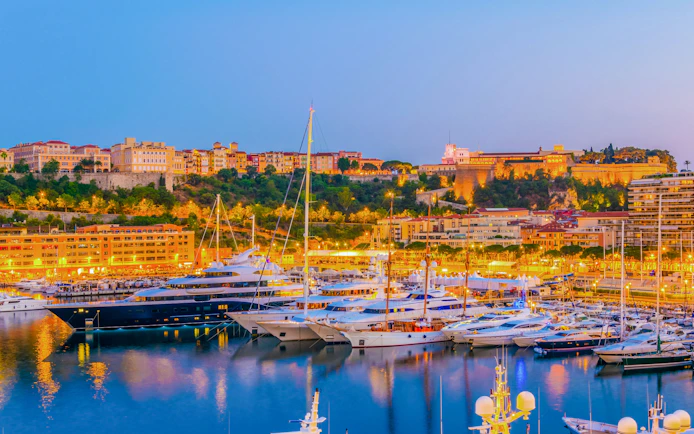 Old Town of Monaco overlooking Port Hercule at sunset with yachts in the harbor.