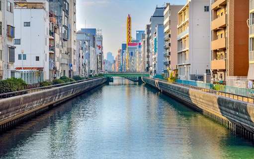 Tombori River Cruise view of Osaka's canal lined with buildings and a distant bridge.