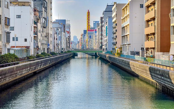 Tombori River Cruise view of Osaka's canal lined with buildings and a distant bridge.