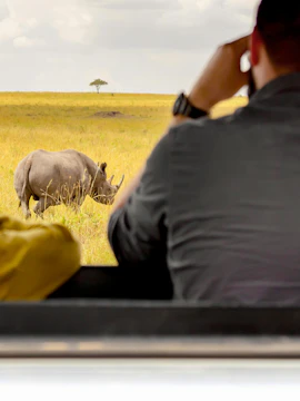 Tourists in safari car observing rhinoceros in Masai Mara National Park, Kenya.