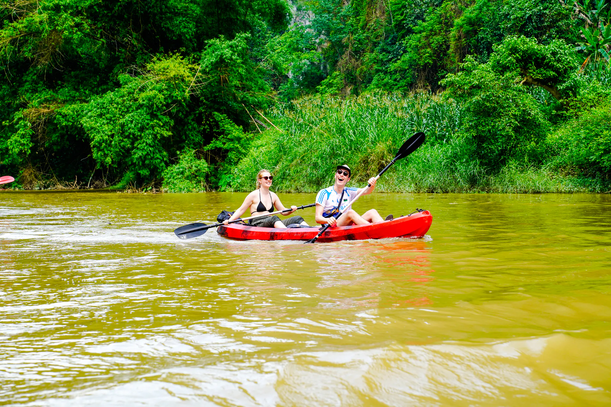 Kayaking on a river surrounded by lush greenery during Ba Be Nature Escape from Hanoi.