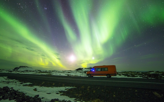 Mini bus under Northern Lights on Icelandic road.