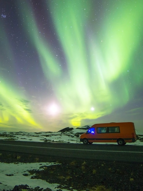 Mini bus under Northern Lights on Icelandic road.