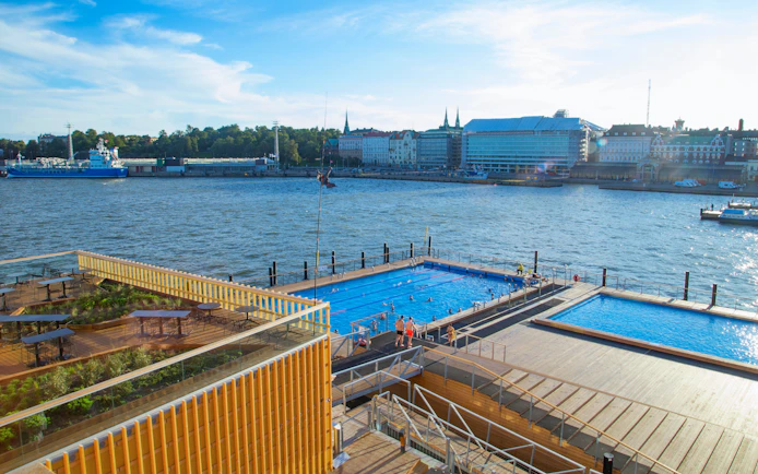 Sea pool at Helsinki port with swimmers and cityscape in the background.