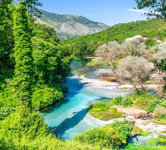 Blue Eye water spring in Albania surrounded by lush greenery and mountains.