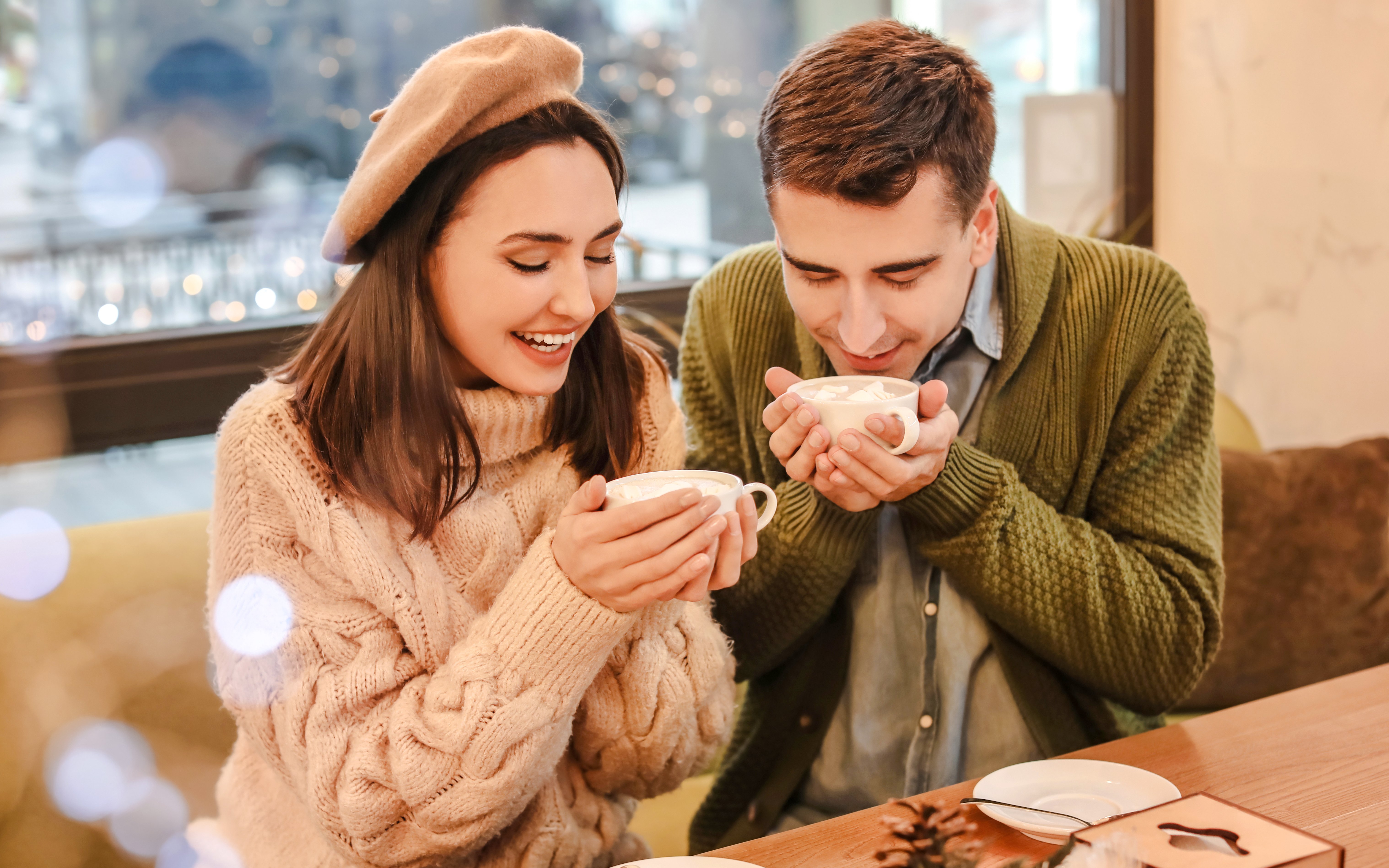 Couple enjoying hot chocolate in a cozy cafe during Christmas.