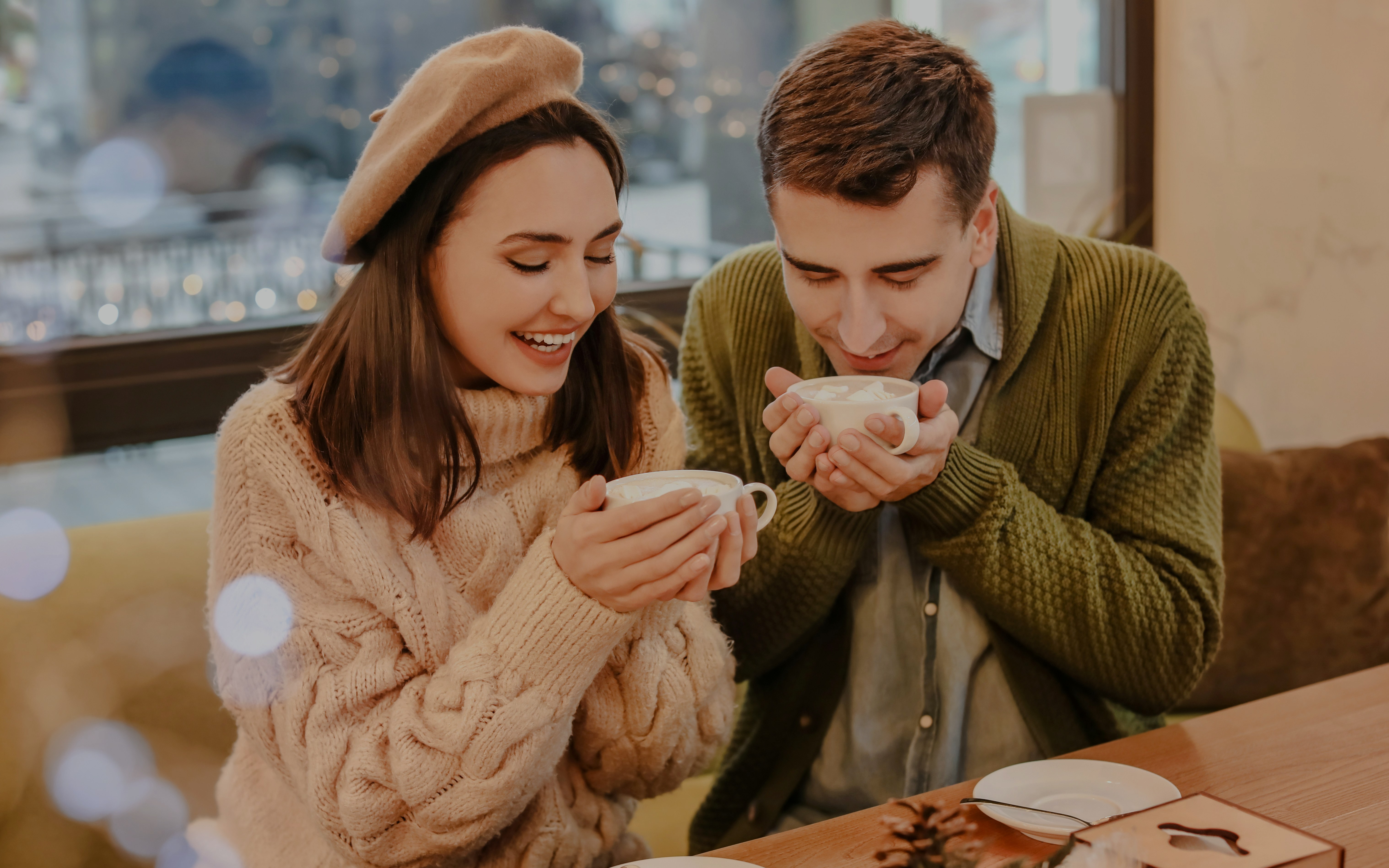 Couple enjoying hot chocolate in a cozy cafe during Christmas.