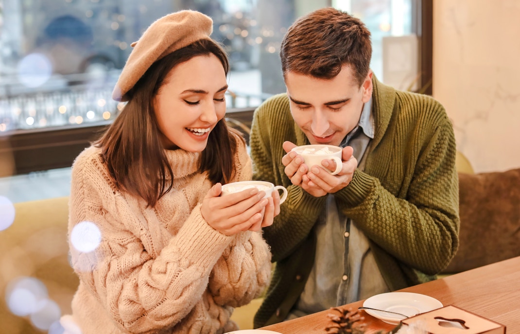 Couple enjoying hot chocolate in a cozy cafe during Christmas.
