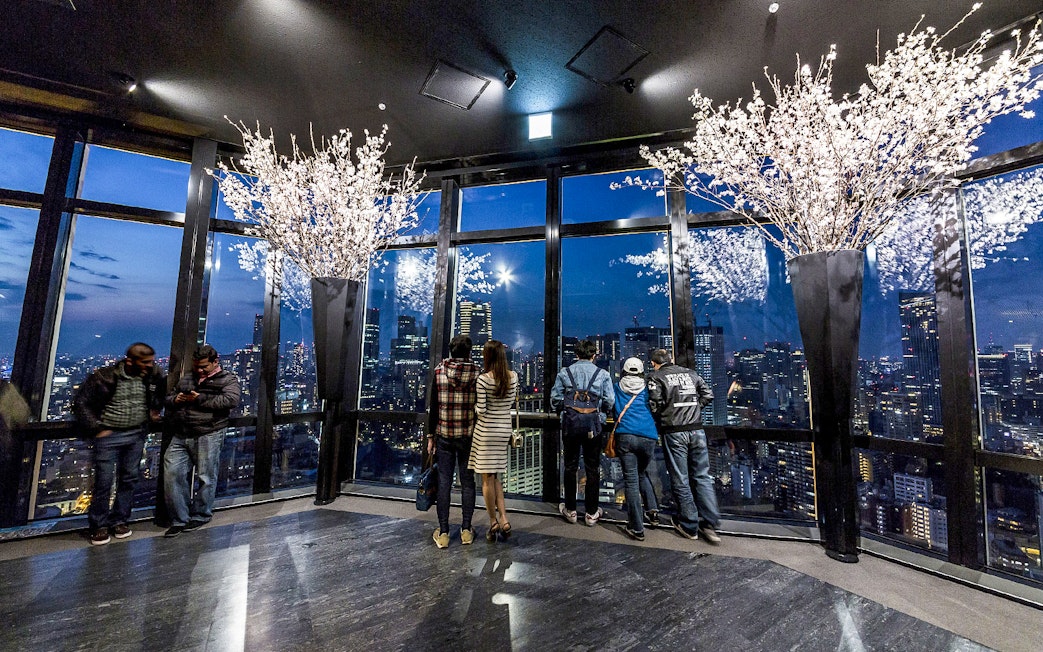 Tokyo Tower observation deck with visitors overlooking city skyline at night.