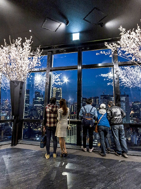 Tokyo Tower observation deck with visitors overlooking city skyline at night.
