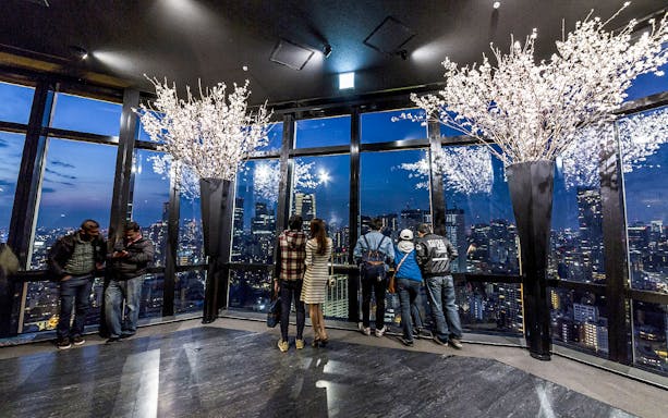 Tokyo Tower observation deck with visitors overlooking city skyline at night.