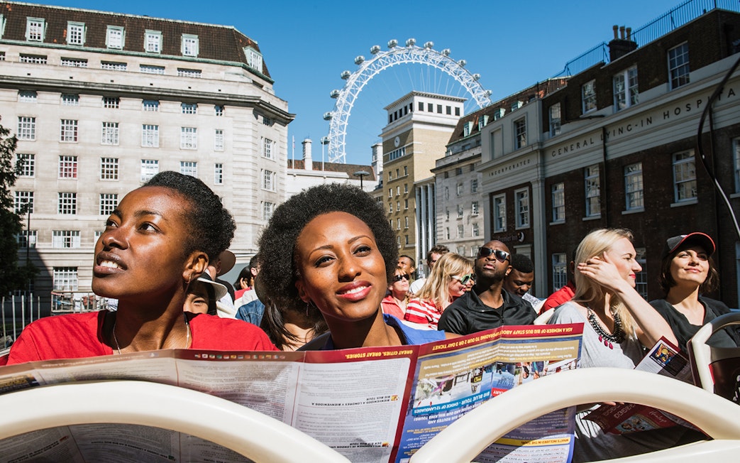 Tourists on BigBus London tour with London Eye in background.