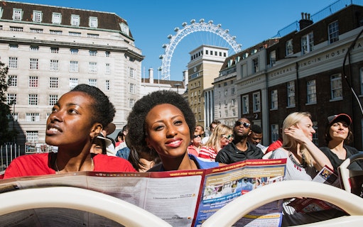 Tourists on BigBus London tour with London Eye in background.