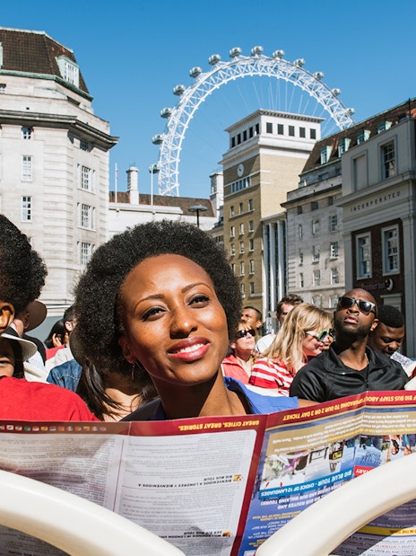 Tourists on BigBus London tour with London Eye in background.