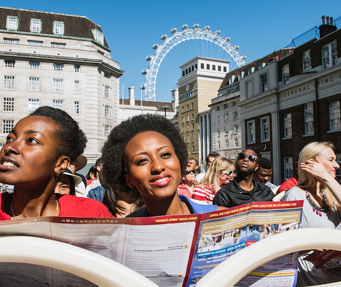 Tourists on BigBus London tour with London Eye in background.