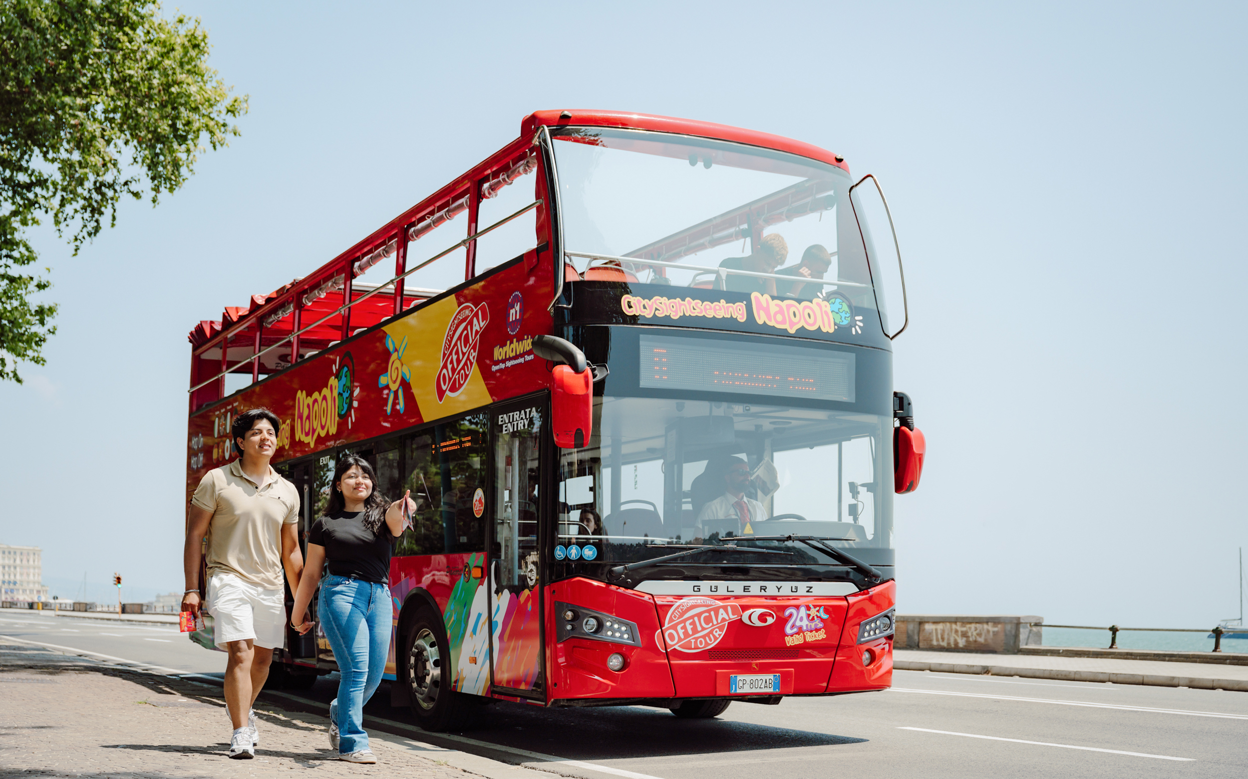 Open-top red bus on City Sightseeing Naples tour with tourists walking nearby.