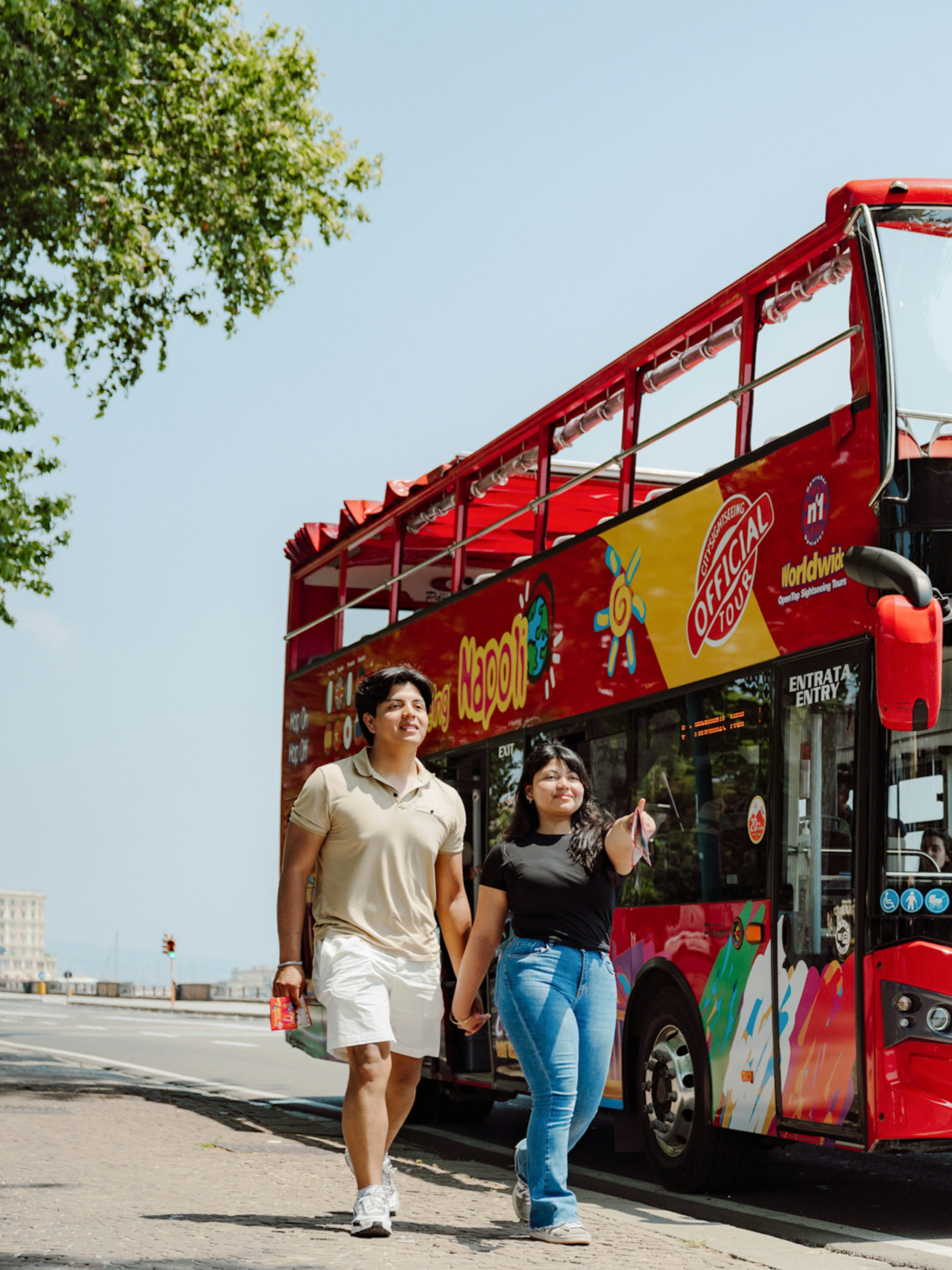 Open-top red bus on City Sightseeing Naples tour with tourists walking nearby.