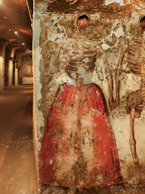 Skeletons in Catacombs of San Gaudioso, Naples, with painted clothing on walls.