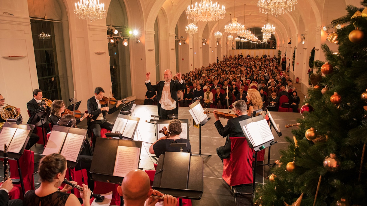 Orchestra performing at Schönbrunn Palace concert with audience and festive decorations, Vienna.