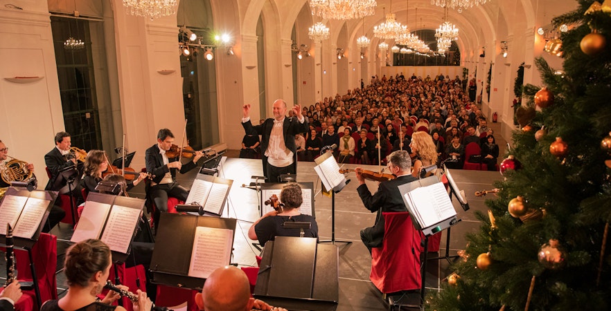 Orchestra performing at Schönbrunn Palace concert with audience and festive decorations, Vienna.