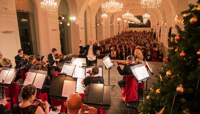 Orchestra performing at Schönbrunn Palace concert with audience and festive decorations, Vienna.
