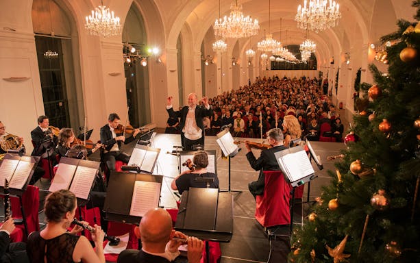 Orchestra performing at Schönbrunn Palace concert with audience and festive decorations, Vienna.