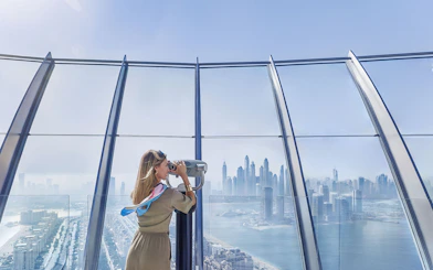 Woman using telescope to view Palm Jumeirah and Dubai skyline.