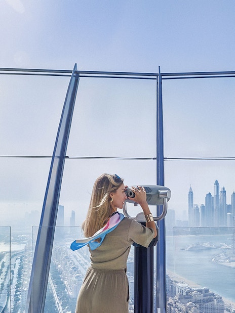 Woman using telescope to view Palm Jumeirah and Dubai skyline.