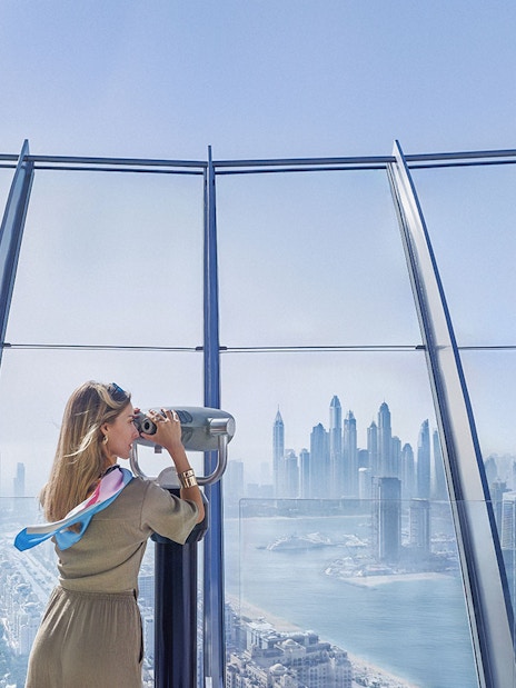 Woman using telescope to view Palm Jumeirah and Dubai skyline.