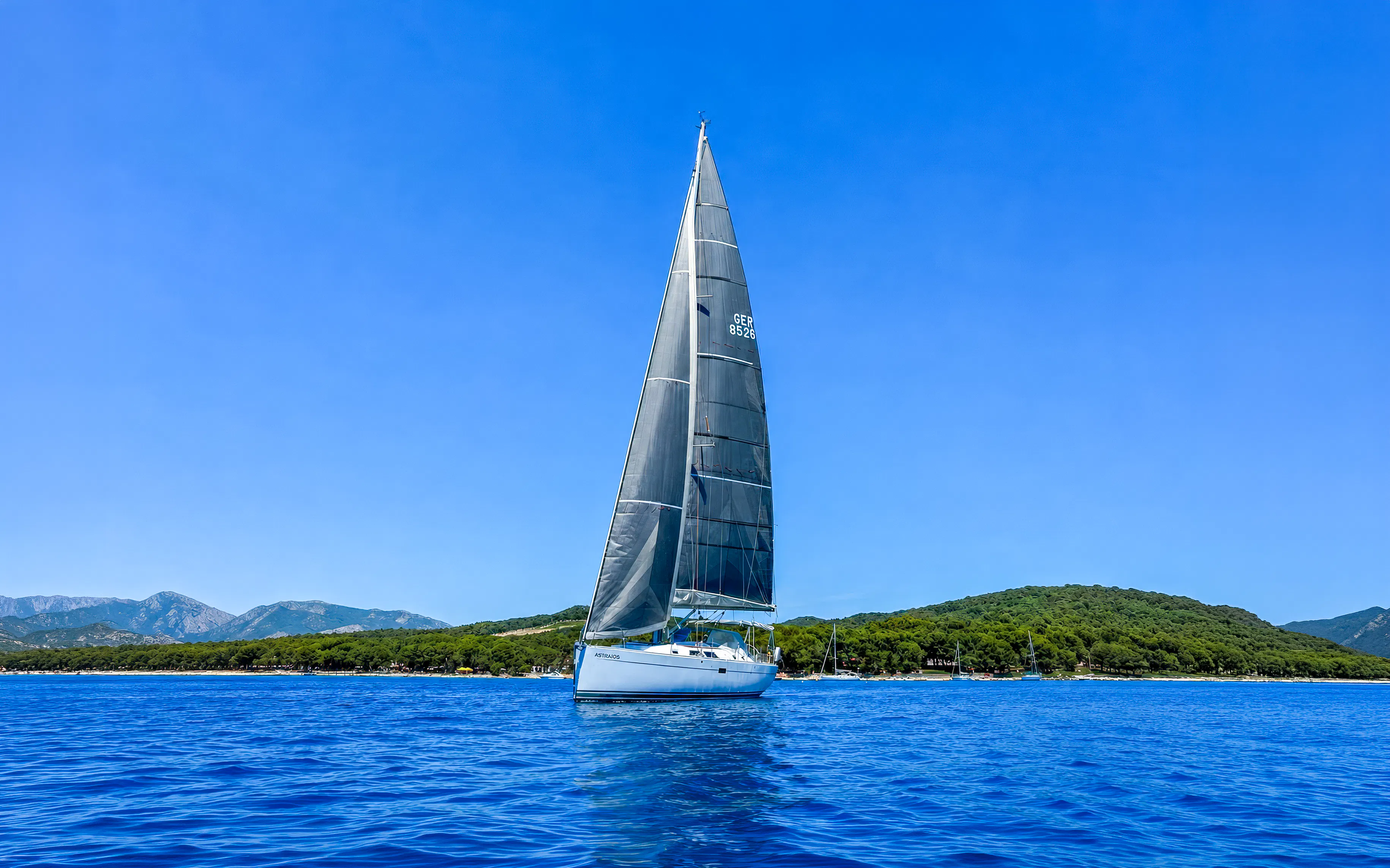 Sailboat on Adriatic Sea near Pula with forested coastline in background.