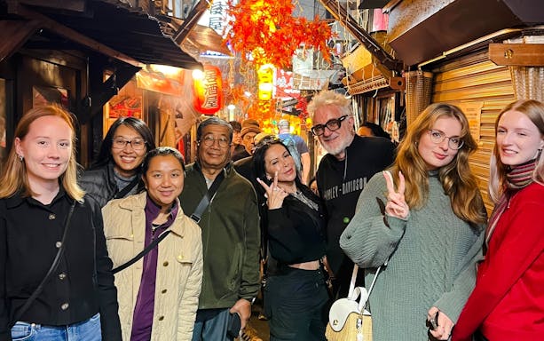 Tourists enjoying Shinjuku food tour in Tokyo, exploring eateries with vibrant street lights.