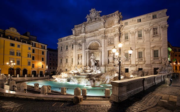 Trevi Fountain illuminated at night in Rome, Italy, with surrounding architecture.