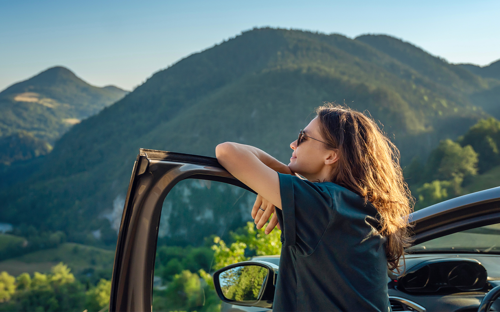 Person enjoying mountain view from car window, ideal for scenic road trips.